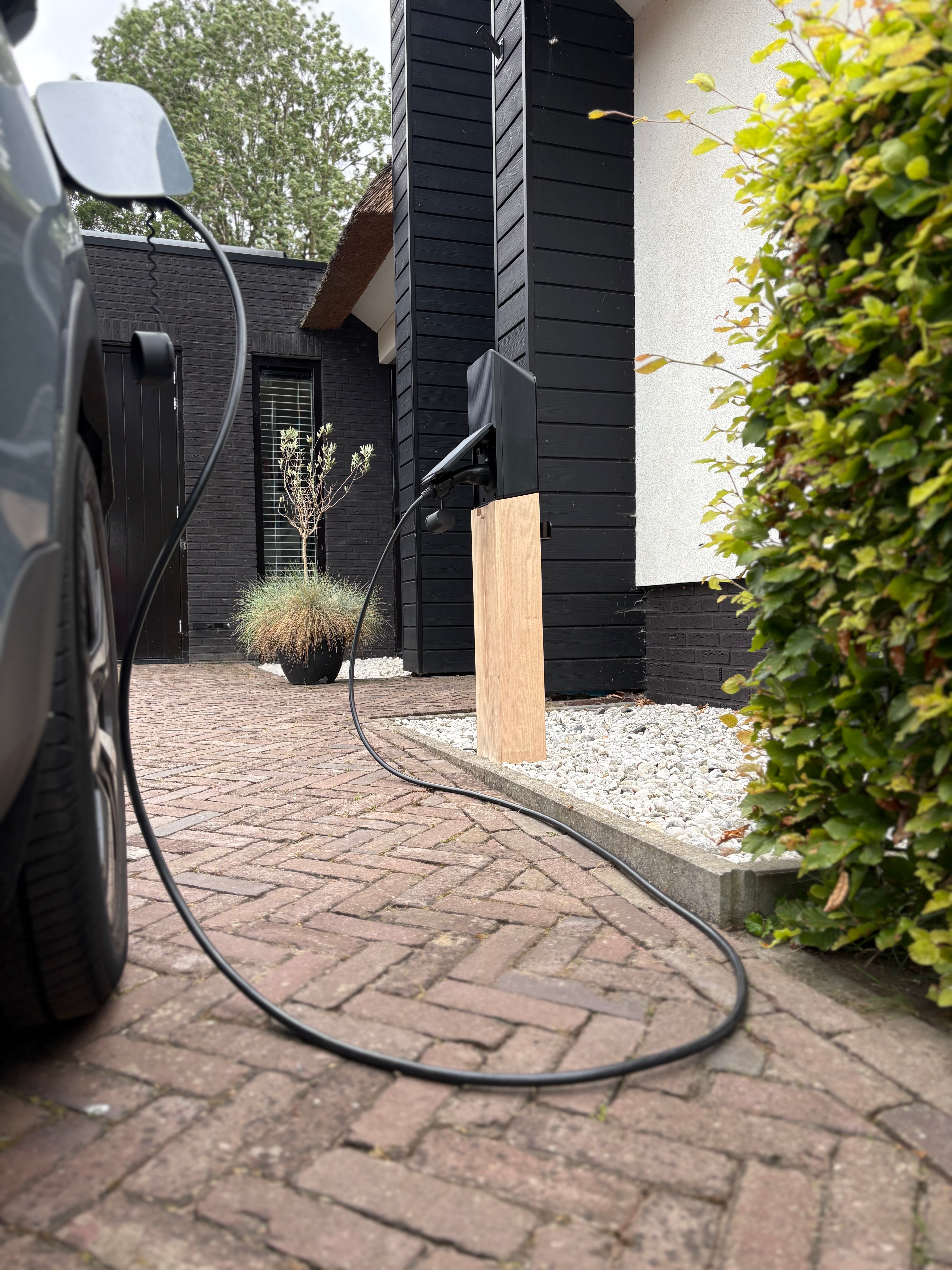 Houten laadpaal met vaste laadkabel naast een elektrische auto